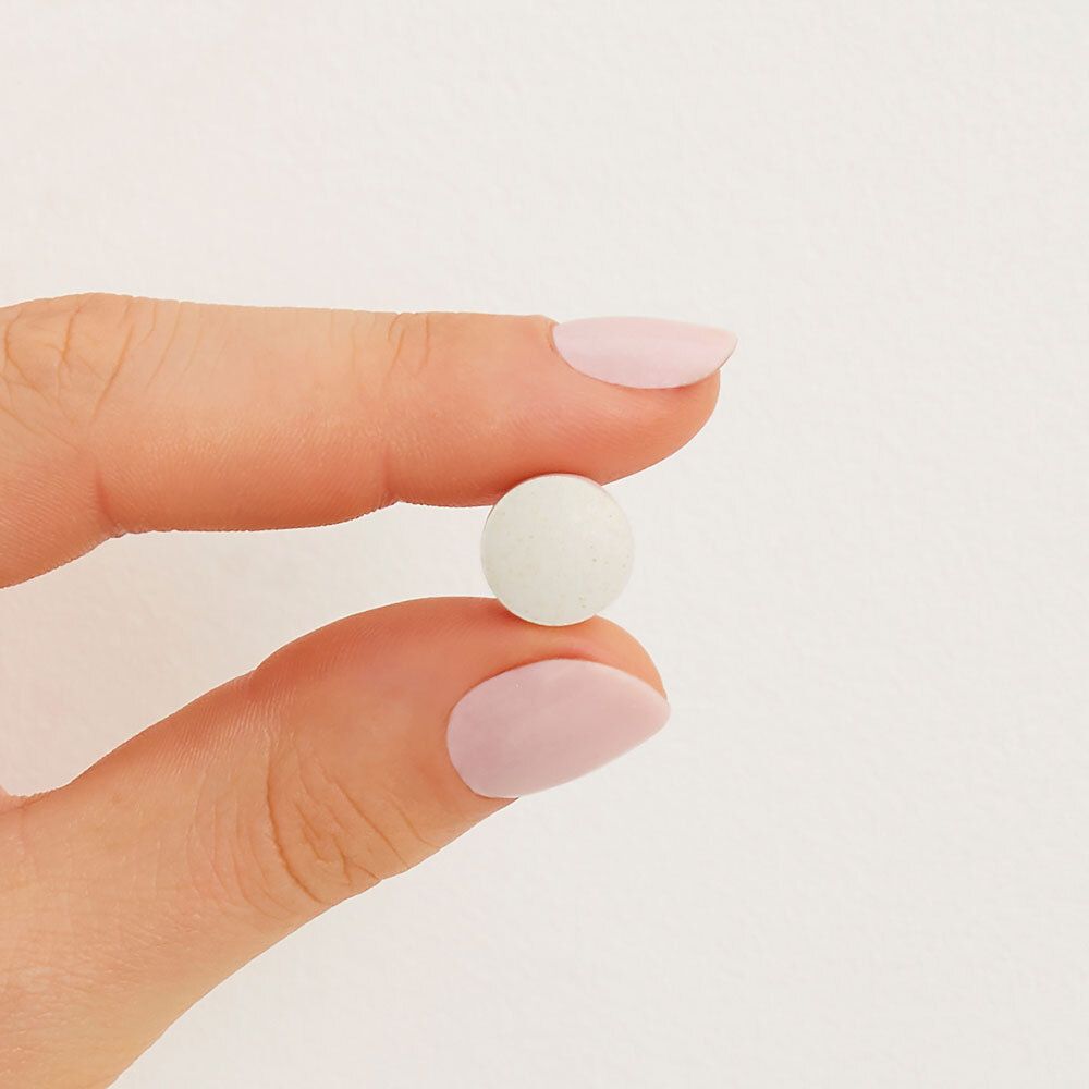 Un seul comprimé rond et blanc, tenu par une main avec des ongles roses vernis.