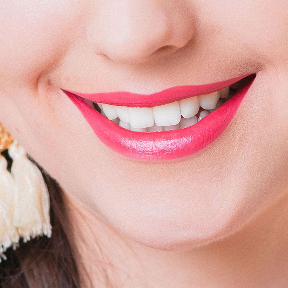 Nahaufnahme eines lächelnden Mundes mit pinkfarbenem Lippenstift. Weiße Zähne sind sichtbar.