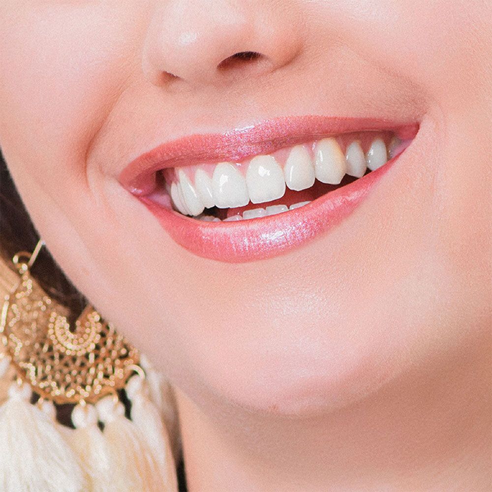 Gros plan sur des lèvres maquillées avec un rouge à lèvres rose. Les lèvres sont légèrement ouvertes, les dents visibles. Boucles d'oreilles dorées.