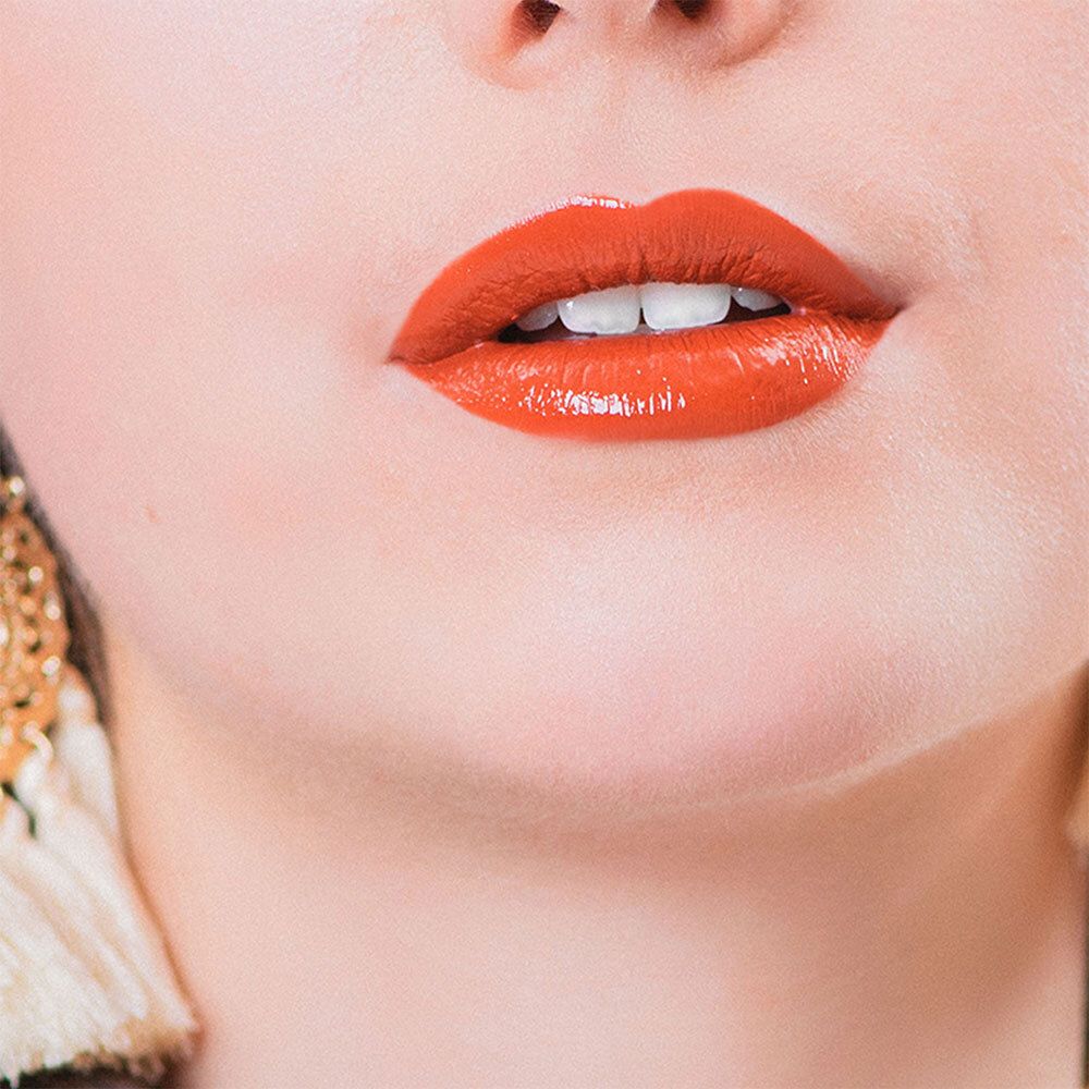 Nahaufnahme von Lippen, die mit einem glänzenden, orangefarbenen Lippenstift geschminkt sind.