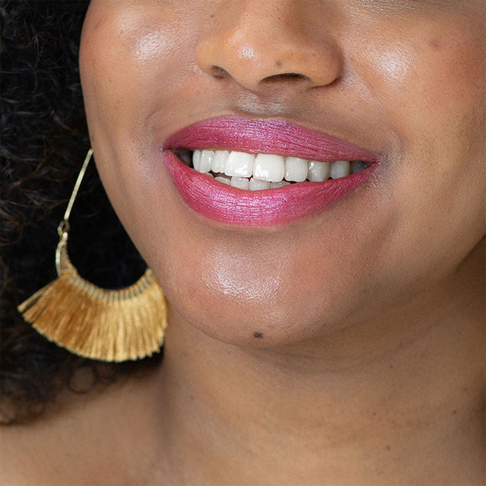 Gros plan sur des lèvres maquillées avec un rouge à lèvres rose. Boucle d'oreille dorée. Teint de peau. Dents.