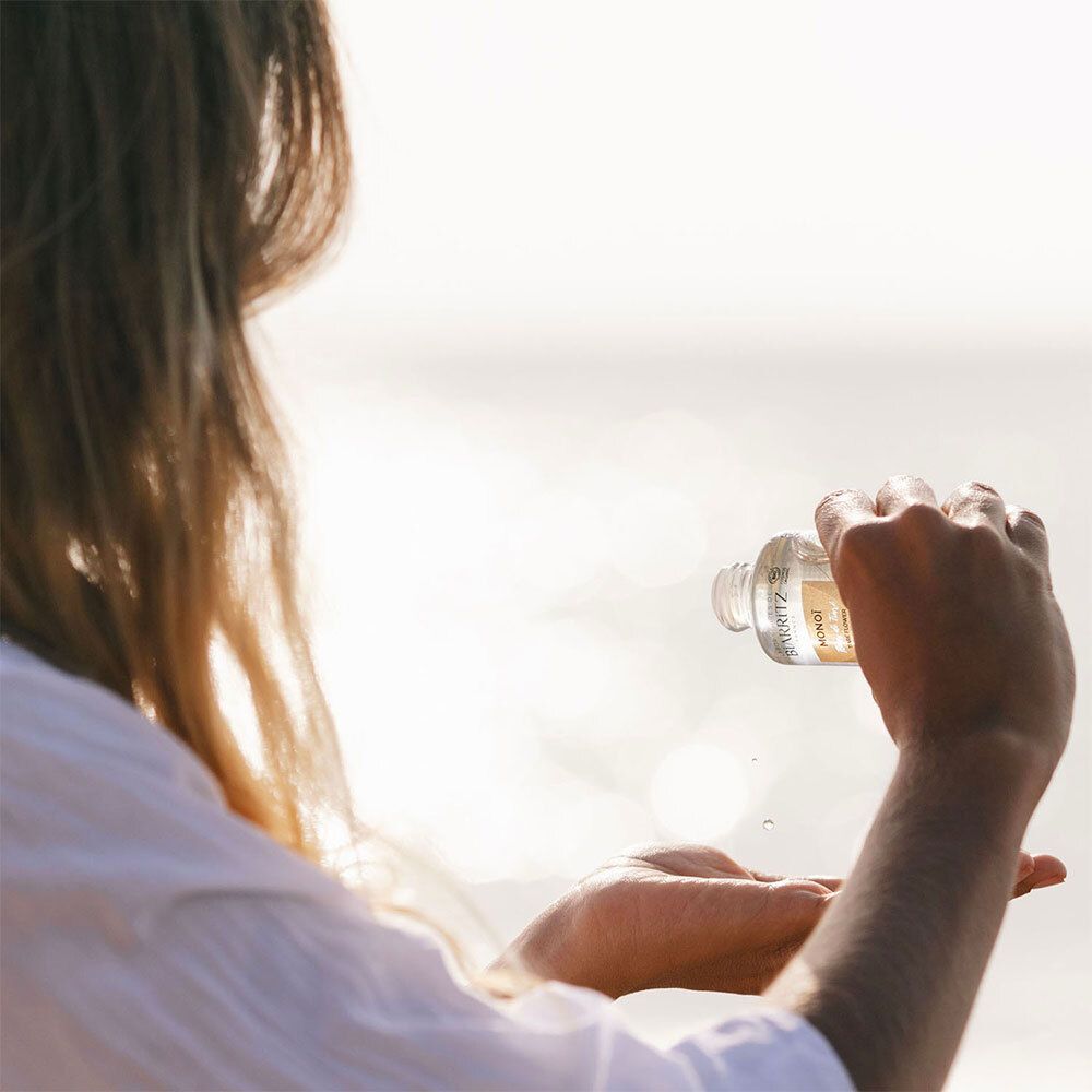 Person gießt Flüssigkeit aus einer Flasche. Flasche mit weißem Deckel. Meer im Hintergrund.