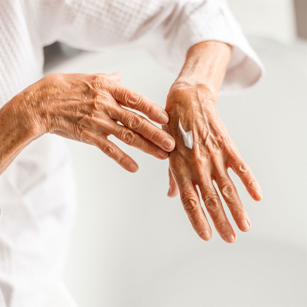 Ältere Hände, die Creme auftragen. Eine kleine Menge Creme auf der Handfläche. Person trägt einen weißen Bademantel.