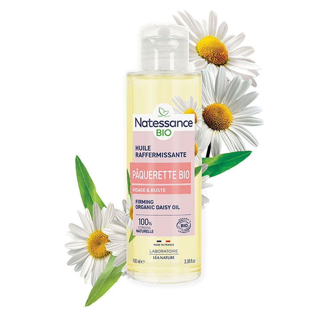 Flacon d'huile Natessance Bio avec marguerites. Fleurs blanches entourent le flacon. Étiquette rose avec texte.