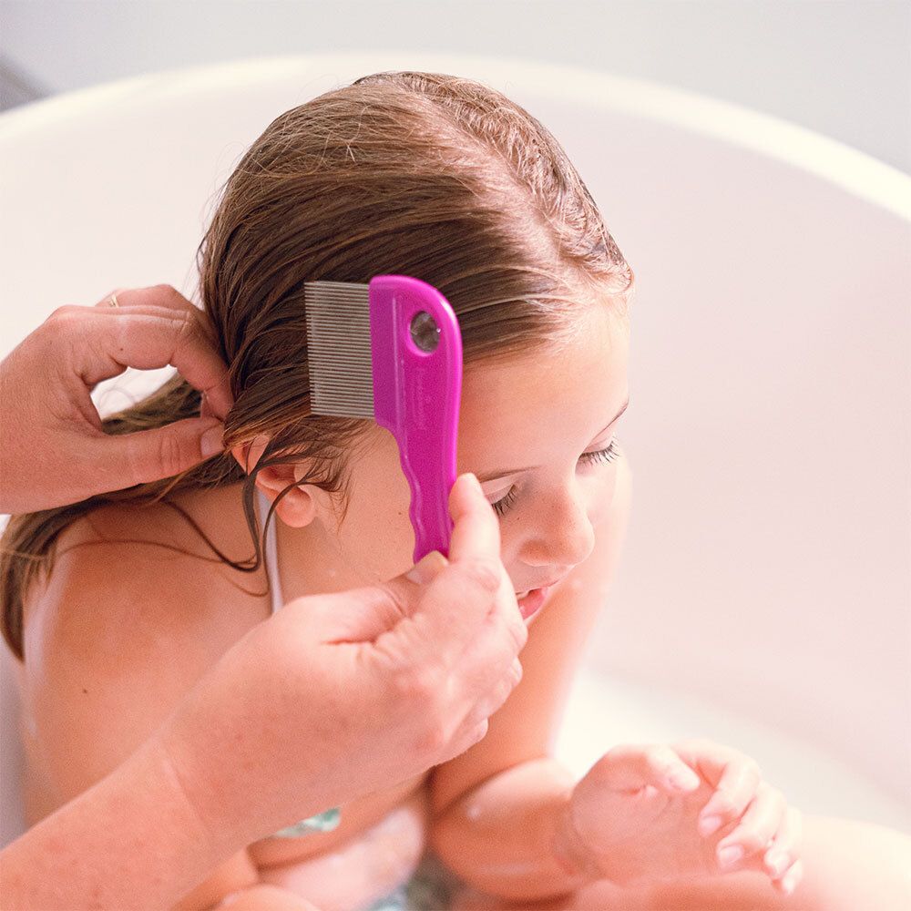 Ein Mädchen in der Badewanne, dem mit einem pinken Kamm die Haare gekämmt werden.
