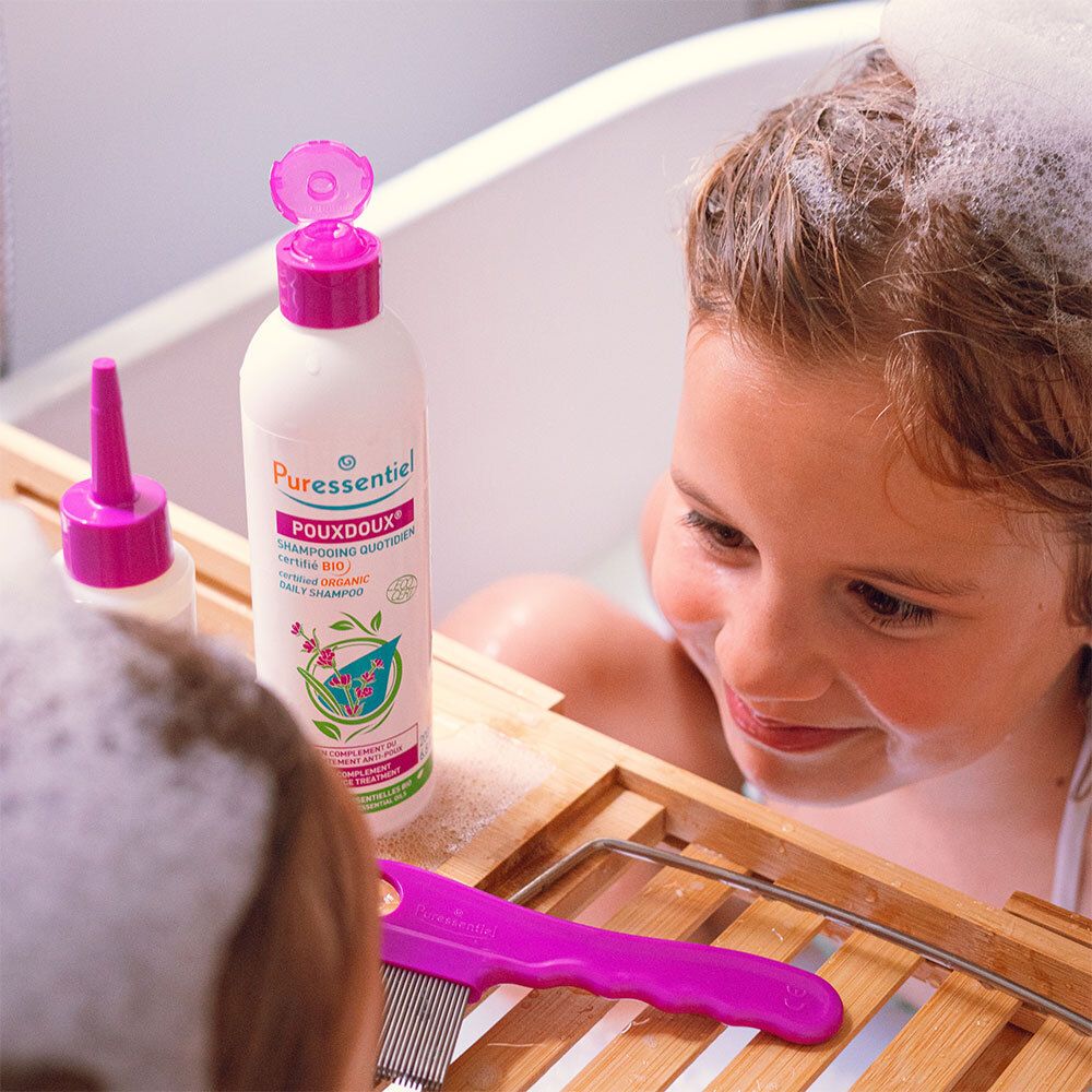 Mädchen in der Badewanne mit Schaum. Daneben Shampoo und Kamm.
