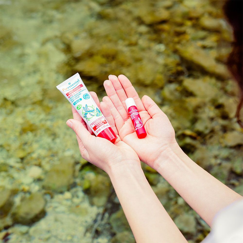 Hände halten Creme-Tube und Lippenbalsam. Creme Anti-Pique für Babys. 30ml. Hintergrund: Wasser.