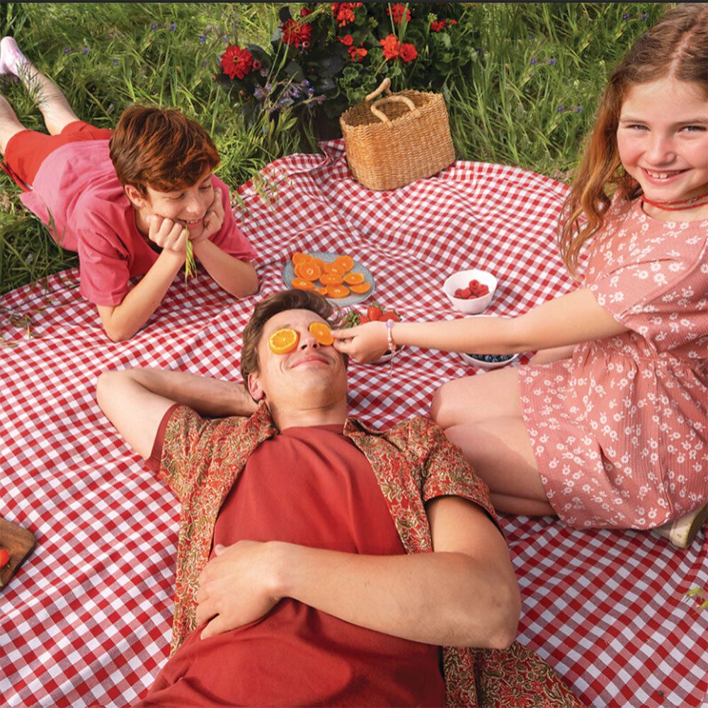 Drei Personen auf einer Picknickdecke. Mann mit Orangenscheiben auf den Augen. Essen und Korb.