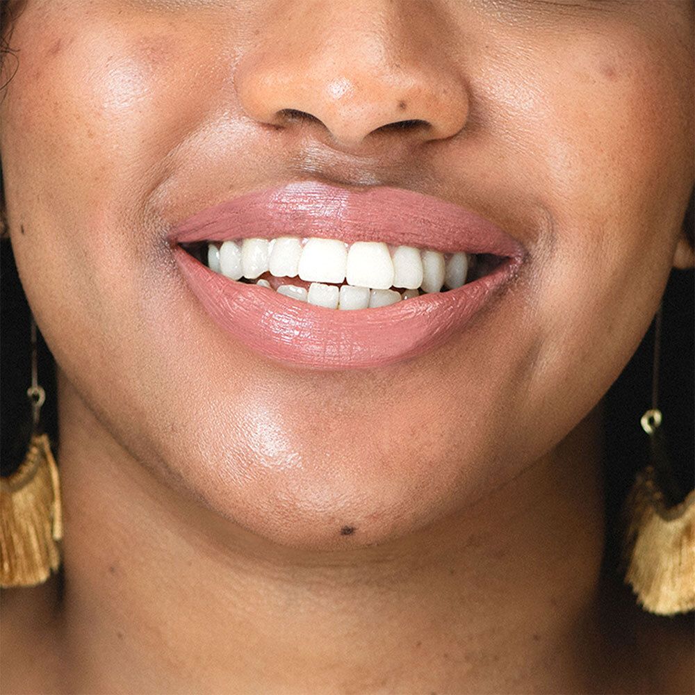 Gros plan d'un visage souriant avec du rouge à lèvres rose. Boucles d'oreilles dorées.