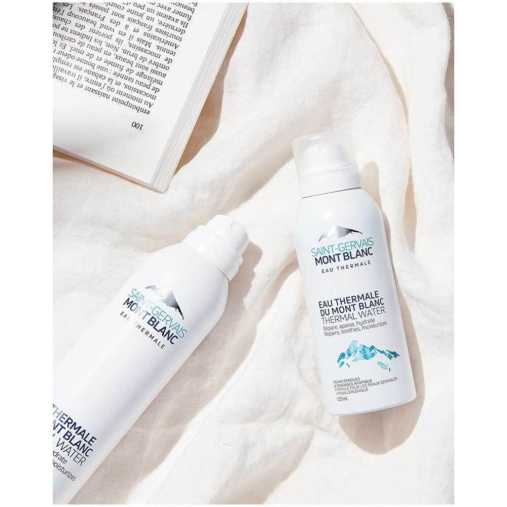 Zwei weiße Sprays mit SAINT-GERVAIS MONT BLANC Logo. Auf weißem Stoff. Ein Buch im Hintergrund.