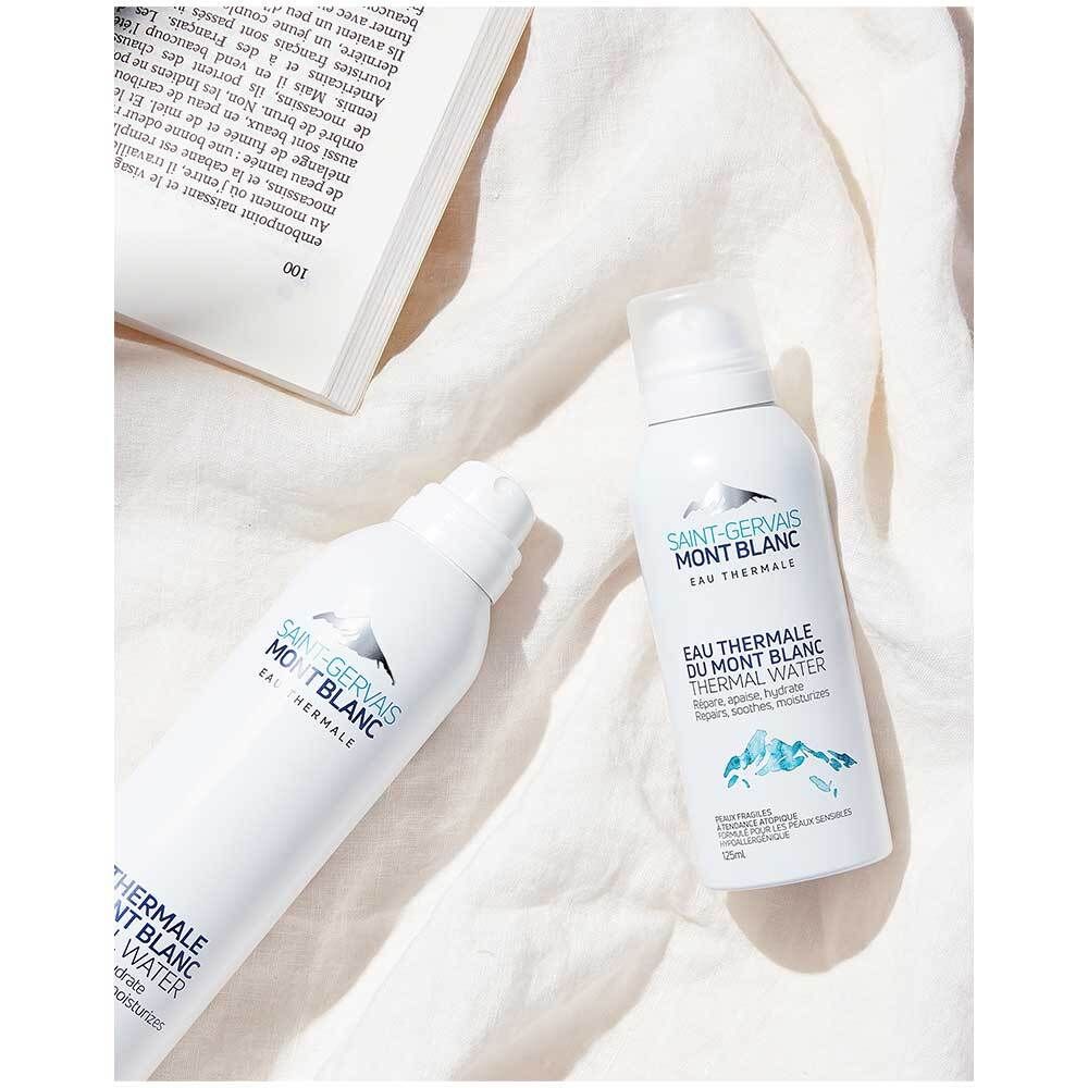 Zwei weiße Sprühflaschen mit blauer Beschriftung. Produktname: Saint Gervais MONT BLANC Thermalwasser. Auf weißem Stoff.