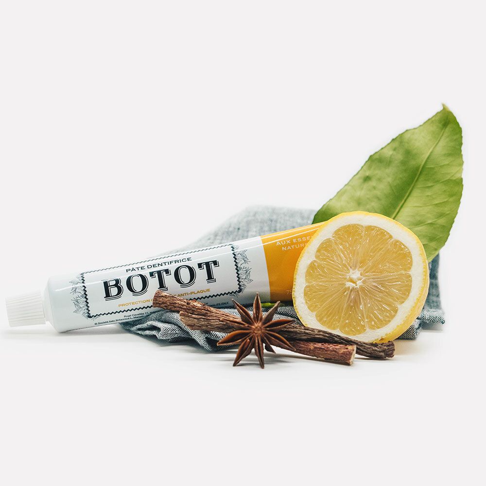 Zahnpasta-Tube, Zitrone, Gewürze und Blatt auf blauem Tuch. Auf der Tube steht BOTOT.