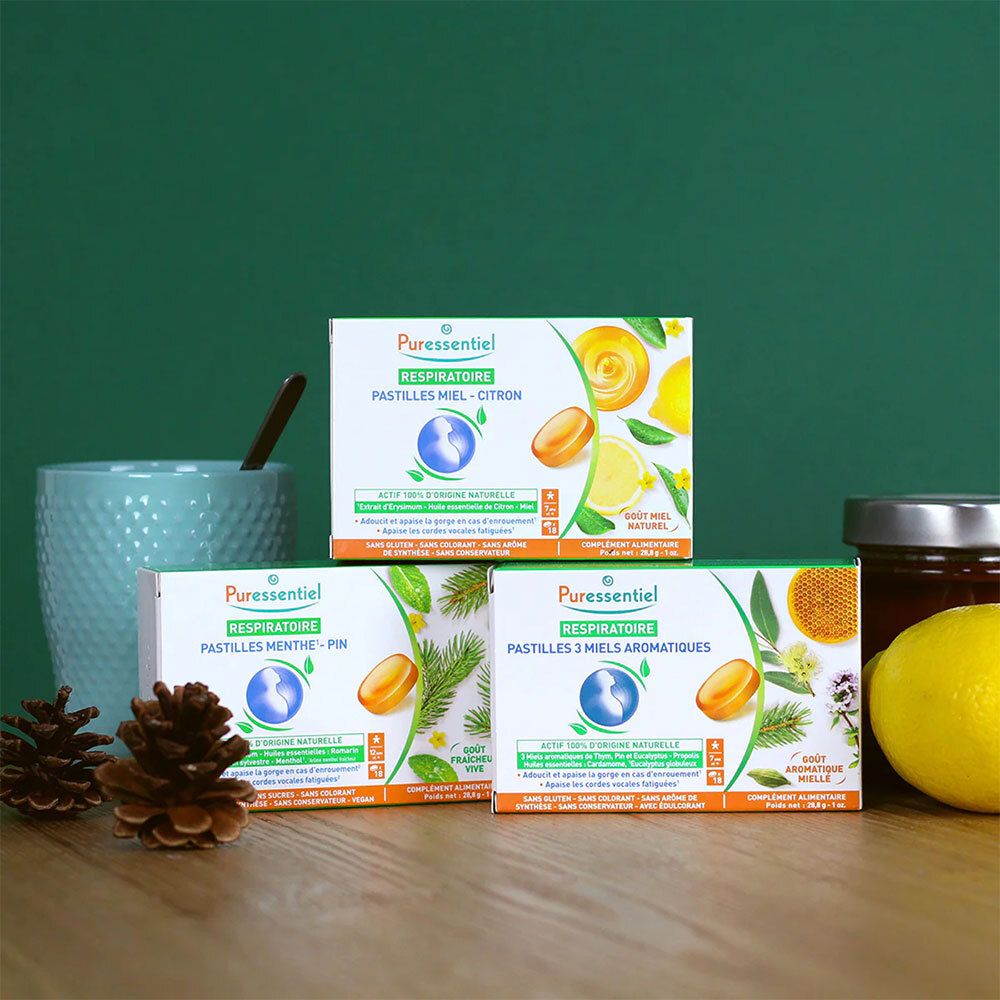 Trois boîtes de pastilles PURESSENTIEL RESPIRATOIRE. Vert, blanc, jaune. Différentes saveurs. Sur surface en bois.