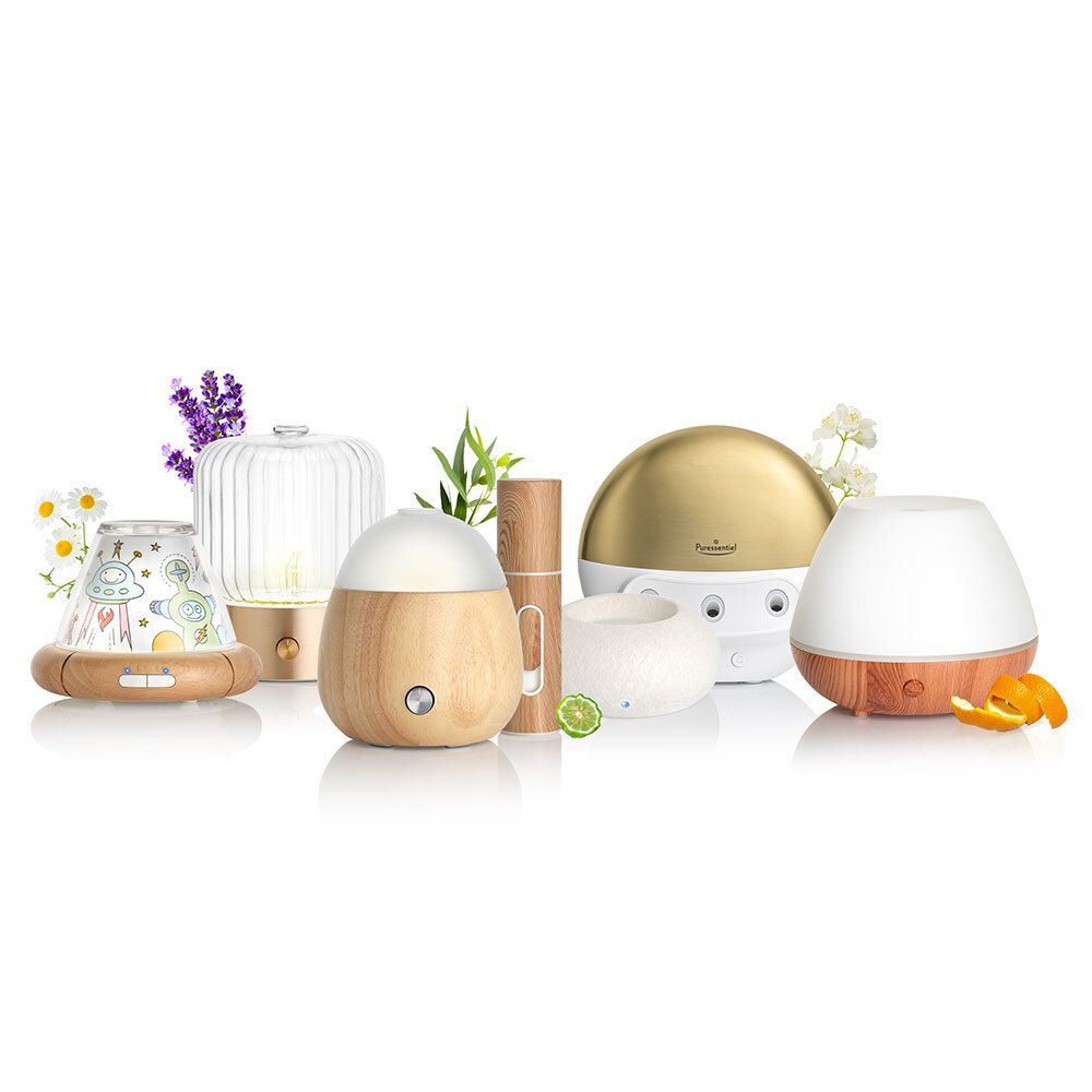 Verschiedene Diffusoren und Flaschen. Aufschrift: Puresentiel. Unterschiedliche Formen und Materialien. Vor Blättern und Blüten.