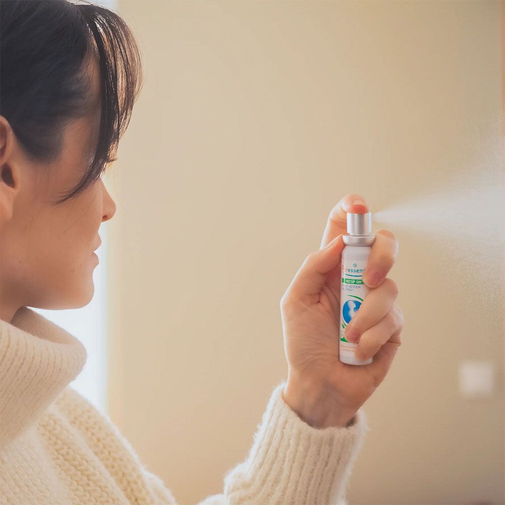 Person hält Puresseentiel Resp'OK® Spray. Weißes Spray mit grünem Deckel, Sprühnebel sichtbar.