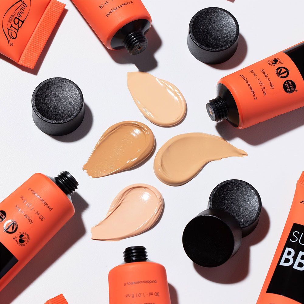 Mehrere Tuben und Farbmuster von BB cream. Tuben orange mit schwarzem Deckel. Farbmuster in verschiedenen Farbtönen.