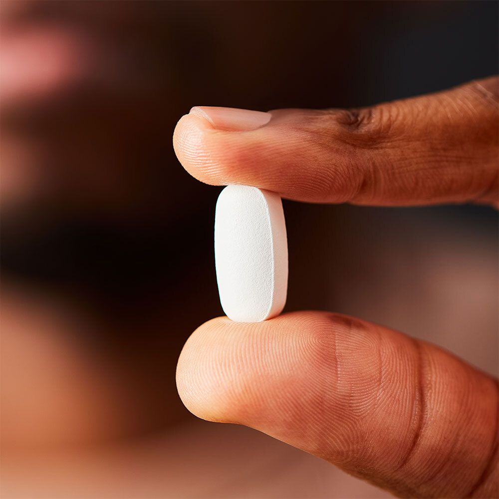 Personne tenant un comprimé blanc ovale entre les doigts. Gros plan.
