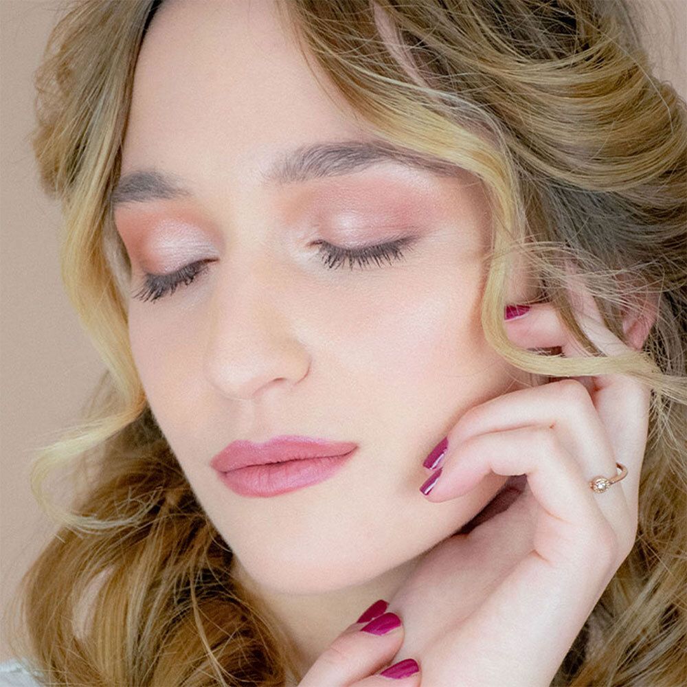 Porträt einer Frau mit geschlossenen Augen. Sie trägt rosa Lidschatten und Lippenstift. Ihre Hand berührt ihr Gesicht.