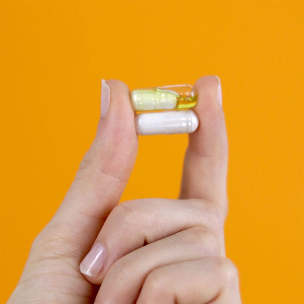 Zwei Kapseln in einer Hand. Gelbe und weiße Kapsel. Orangefarbener Hintergrund.