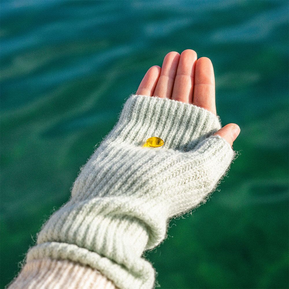Hand mit einer gelben Pastille in einer grauen Handschuh. Hintergrund: Wasser.