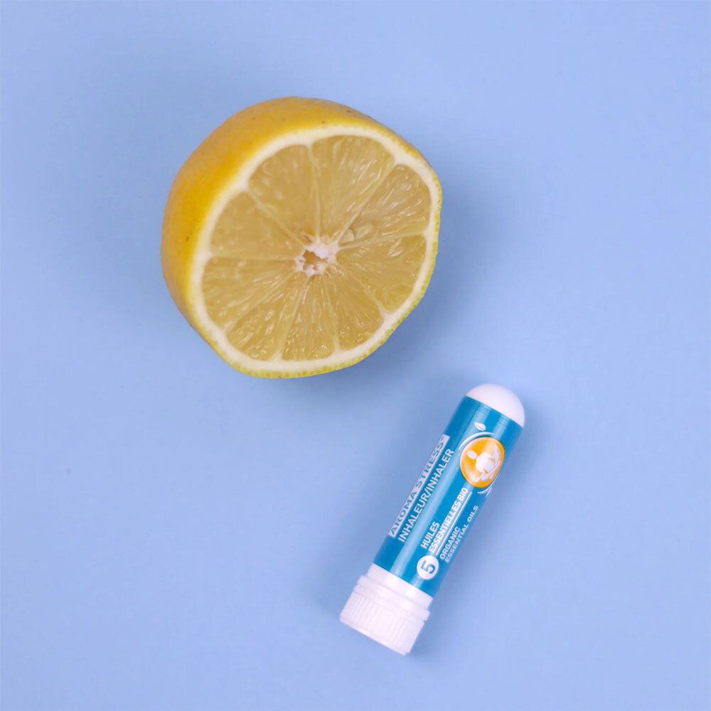 Ein Puressentiel AROMA STRESS® Inhalator neben einer halbierten Zitrone. Aufschrift: AROMA STRESS® Inhaler/Inhalator.