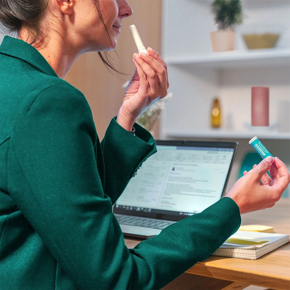 Eine Frau hält einen Puressentiel AROMA STRESS® Inhalator. Auf dem Tisch ein Laptop und ein weiterer Inhalator.