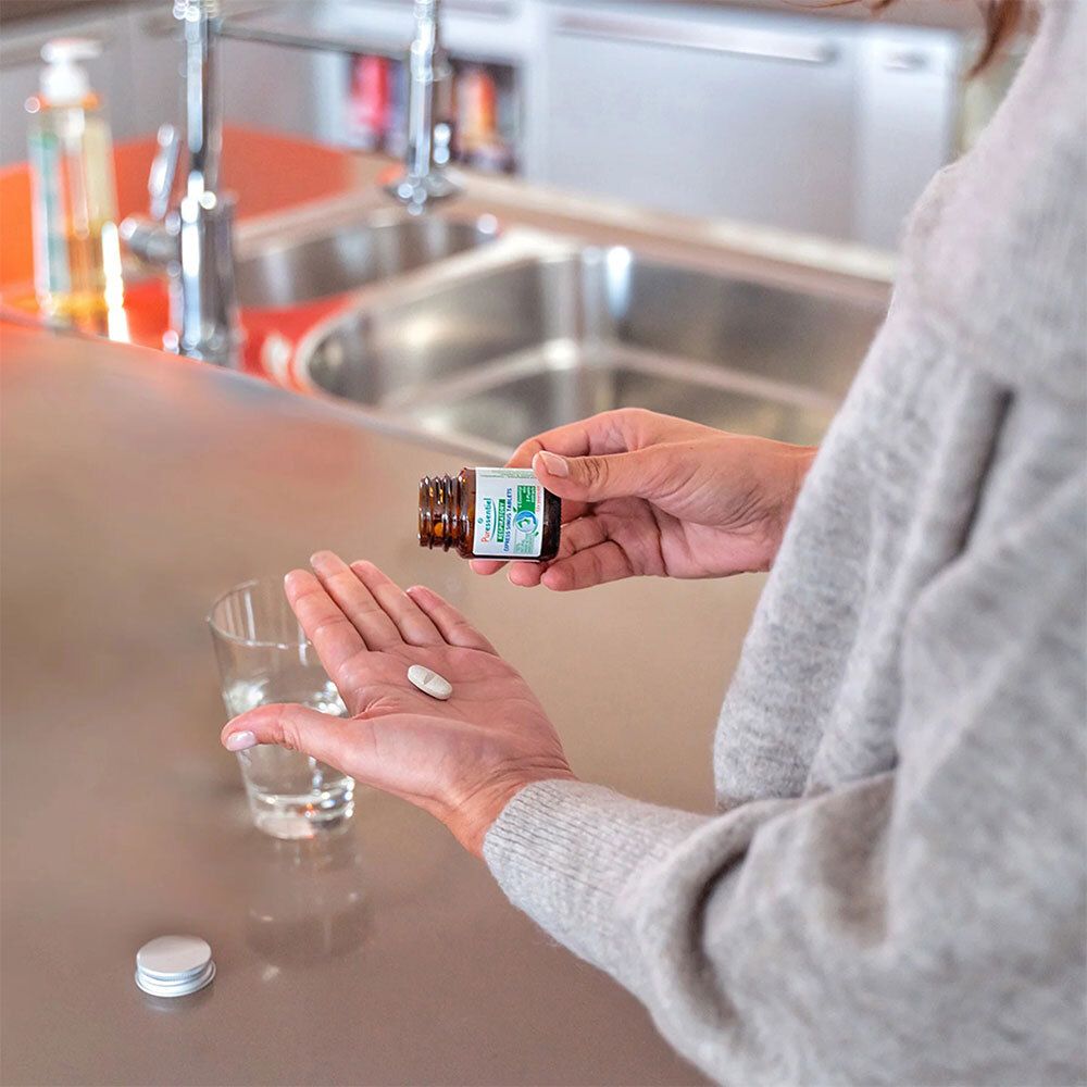 Frau hält braune Glasflasche und Tablette. Aufschrift: Puressentiel RESPIRATORISCH / RESP OK® Sinus Express Tabletten. Glas Wasser.