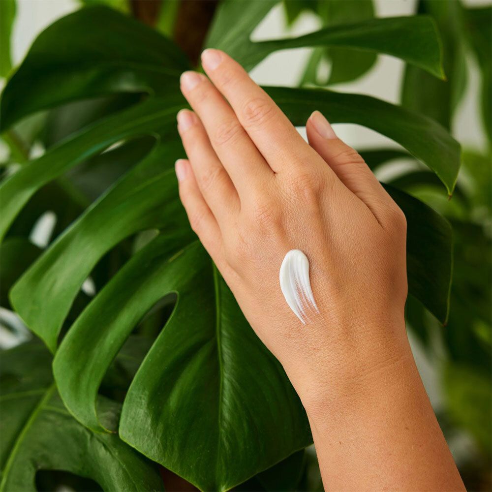 Main avec crème sur une feuille verte. Application de crème sur la main.