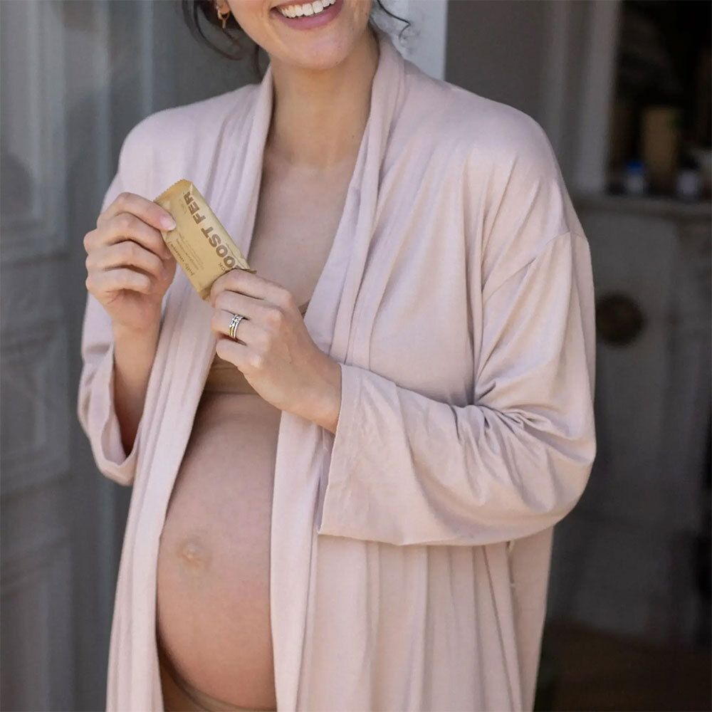 Schwangere Frau hält eine kleine, rechteckige Verpackung. Aufdruck: „BOOST FER“.