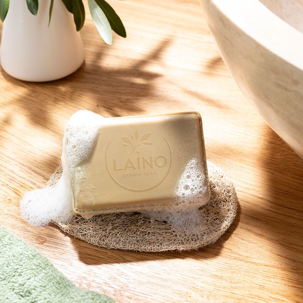 Savon avec mousse sur une éponge. Logo LAINO visible. Surface en bois en arrière-plan.
