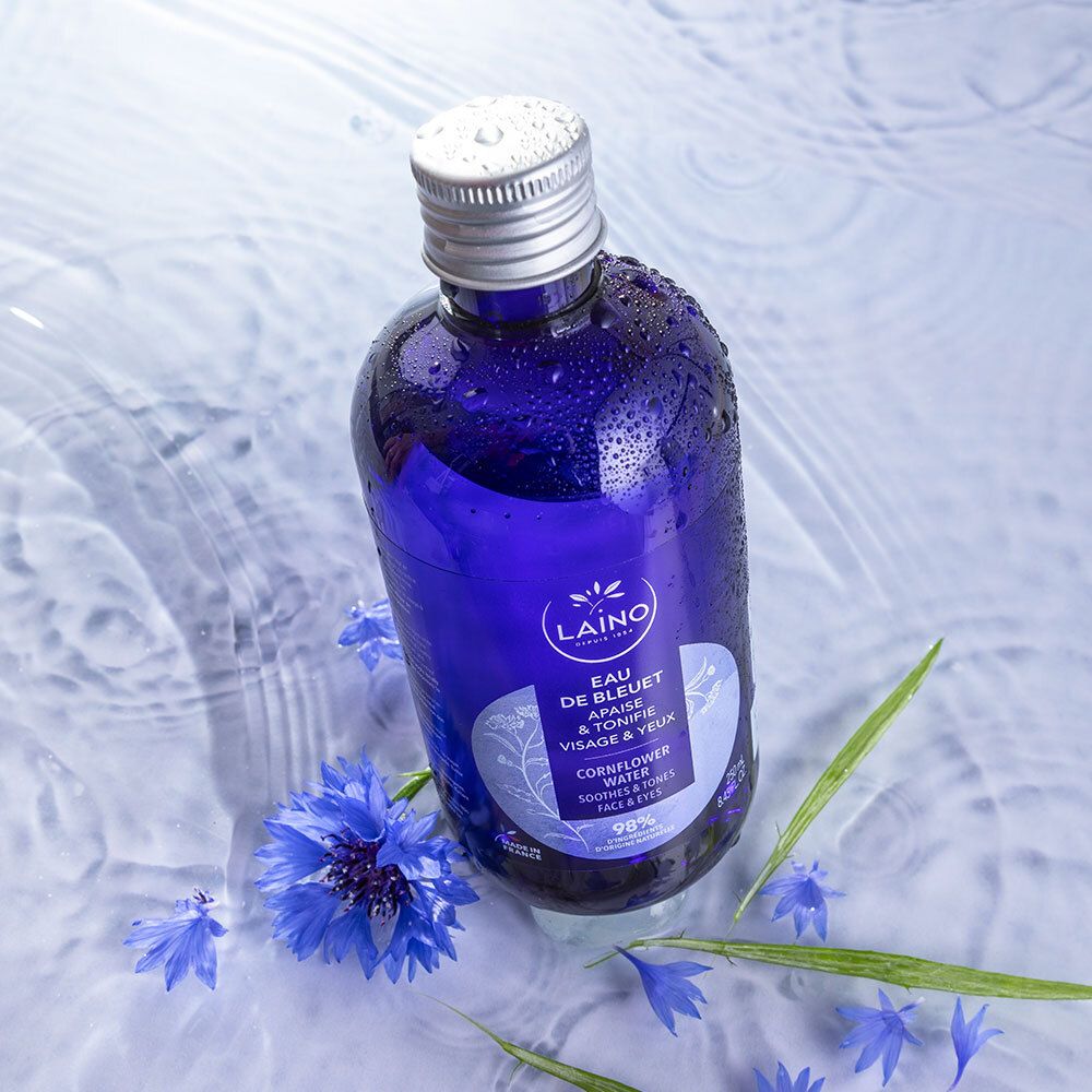 Flacon bleu LAINO Eau de Bleuet dans l'eau. Fleurs de bleuet et feuilles vertes entourent le flacon. Bouchon argenté.