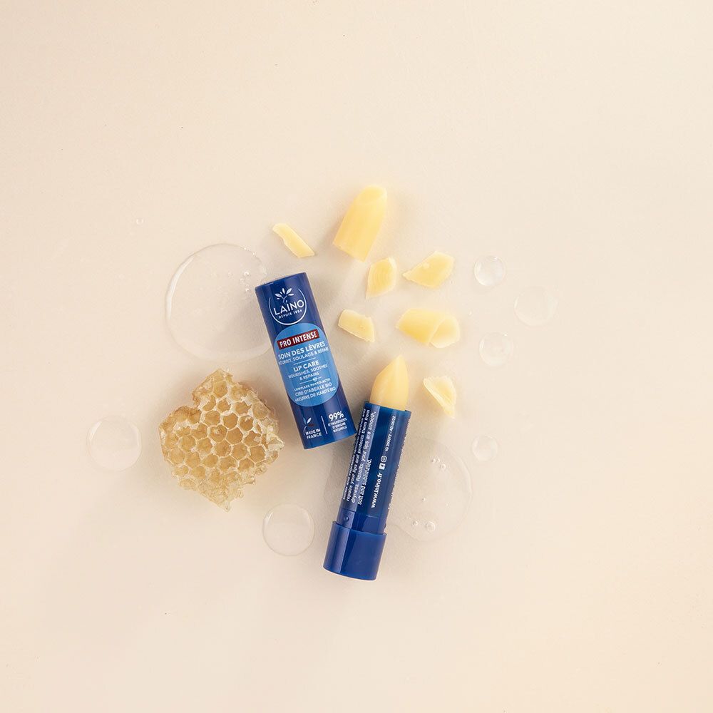 Deux sticks de soin des lèvres bleus LAINO, à côté d'un rayon de miel et morceaux de cire. Sur fond crème.