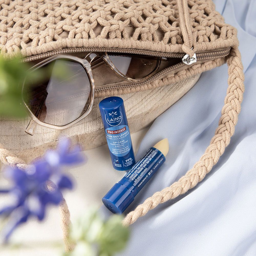 Deux sticks de soin des lèvres bleus LAINO dans un sac beige. Lunettes de soleil à côté. Fleur bleue au premier plan.