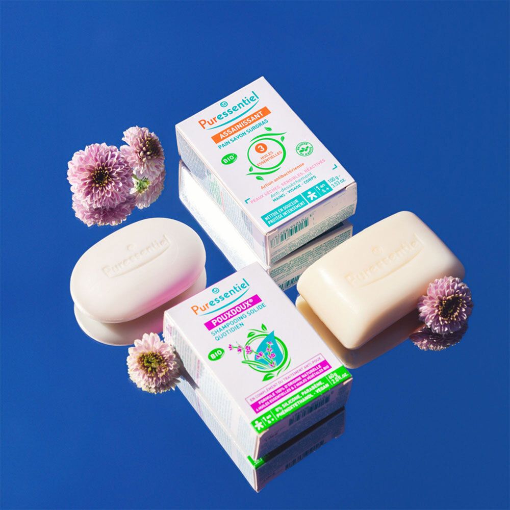 Trois emballages de shampooing Puressentiel Pouxdoux® et deux shampooings sur fond bleu.