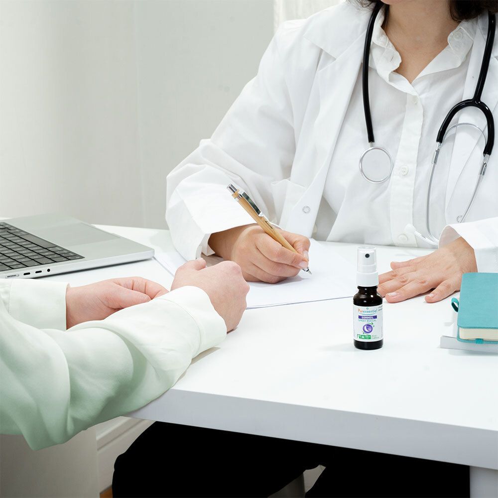 Arzt und Patient mit brauner Glasflasche mit weißem Sprühkopf auf dem Tisch. Aufschrift: PURESSENTIEL Sommeil Spray bukkal.
