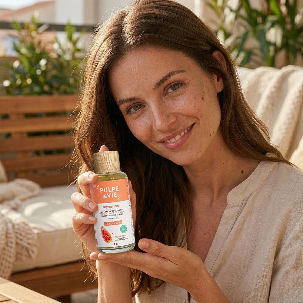 Frau hält eine Flasche. Aufschrift: PULPE de VIE, Nutrition. Holzfarbener Verschluss. Frau lächelt.