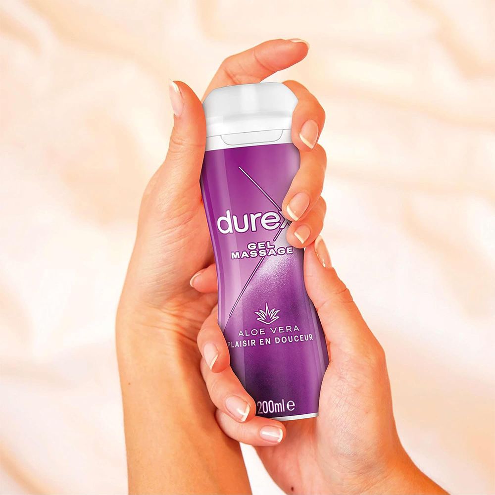 Mains tenant une bouteille de gel de massage Durex. Bouteille violette avec bouchon blanc. Texte: Aloe Vera, Plaisir en douceur.