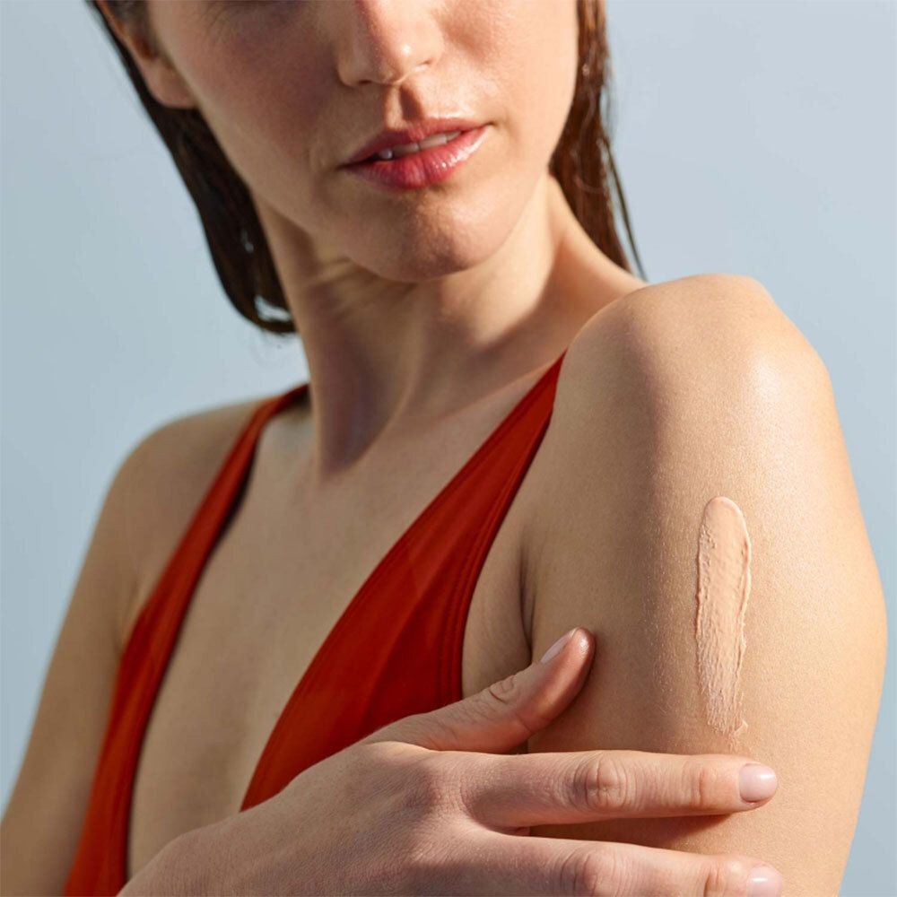 Arm mit aufgetragener Sonnenschutzmilch. Creme-Farbe. Frau mit rotem Oberteil.