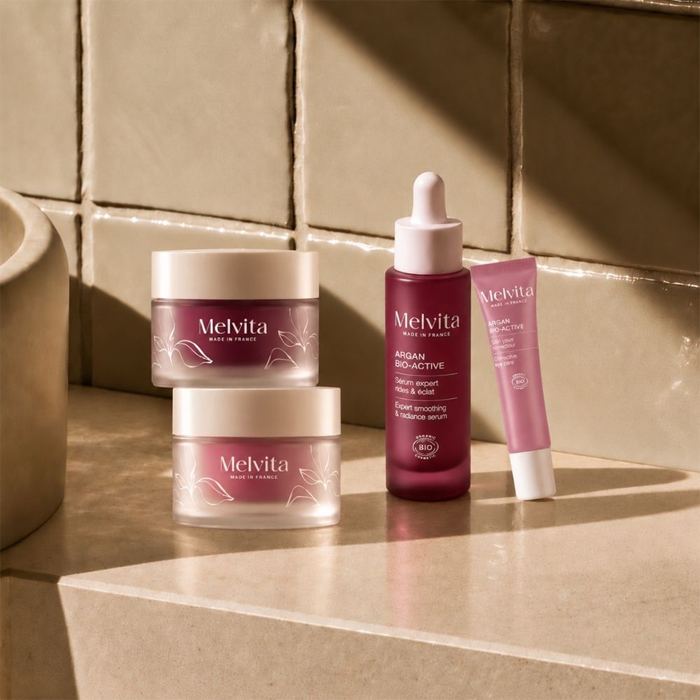 Ein Melvita Argan Bio-Active Serum mit Pipette, zwei Melvita Tiegel und eine Melvita Tube auf einer hellen Oberfläche.