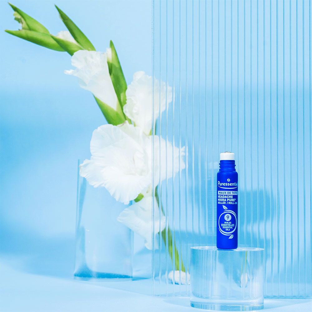 Blaues Roll-on. Marke: Puressentiel. Text: Maux de tête. Auf Glasplatte vor Blumen.