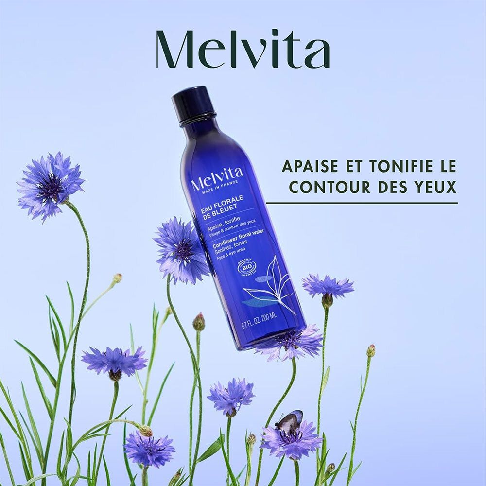 Melvita Eau Florale de Bleuet-Flasche, umgeben von blauen Kornblumen. Text: Apaise et tonifie le contour des yeux.