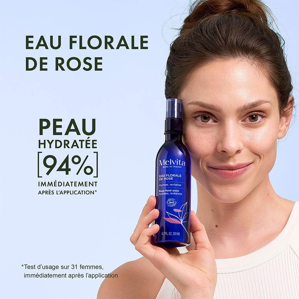 Femme tenant un flacon pulvérisateur bleu. Texte: Eau Florale de Rose, Peau Hydratée [94%].