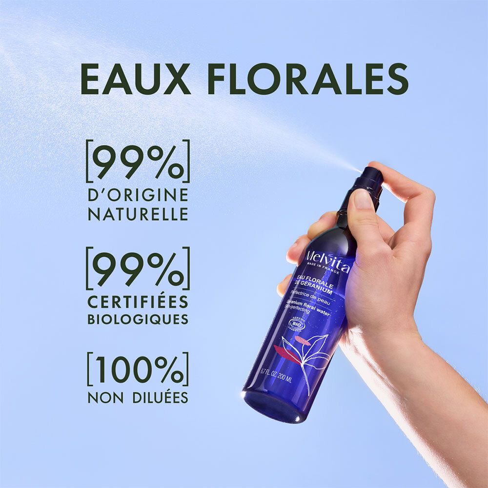 Main vaporisant d'une bouteille bleue. Texte: Eaux Florales, [99%] naturel, [99%] bio, [100%] non dilué.