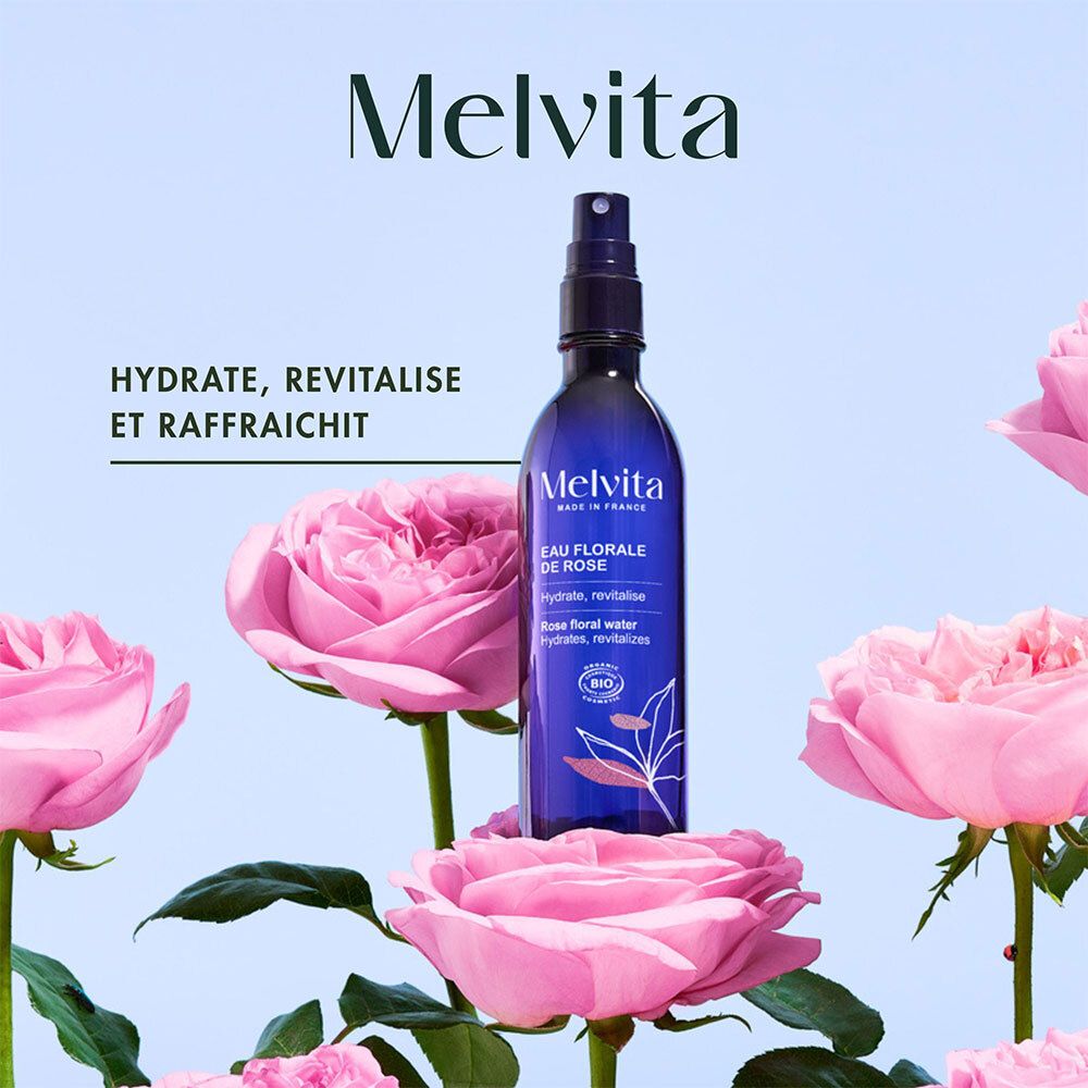 Blau-transparente Flasche mit Sprühkopf, umgeben von rosa Rosen. Aufschrift: Melvita, Eau Florale de Rose. Bio-Zertifizierung.