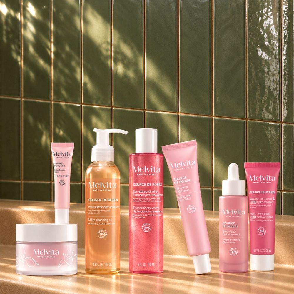 Eine Reihe von Melvita Hautpflegeprodukten in rosa und orangefarbenen Flaschen und Tiegeln.