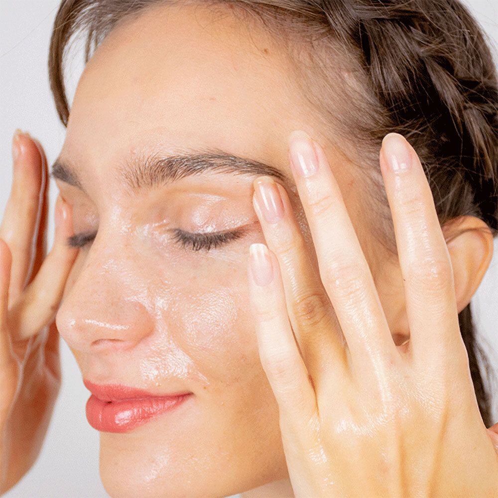 Femme aux yeux fermés appliquant de l'huile sur son visage. Mains sur les yeux. Gros plan.