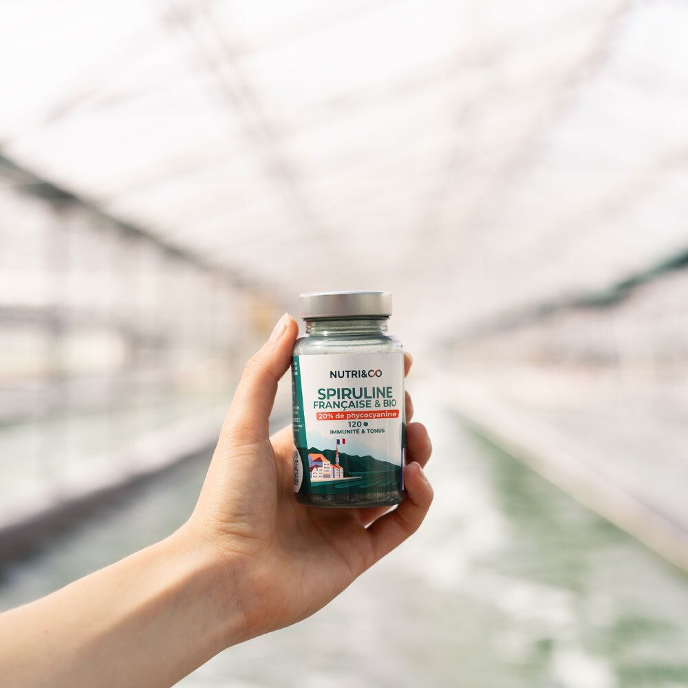 Main tenant un flacon de Spiruline Française & Bio. 20% phycocyanine, 120 comprimés. Drapeau français.