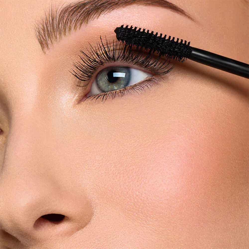 Nahaufnahme eines Auges, das mit einer Mascarabürste geschminkt wird. Schwarze Wimperntusche.