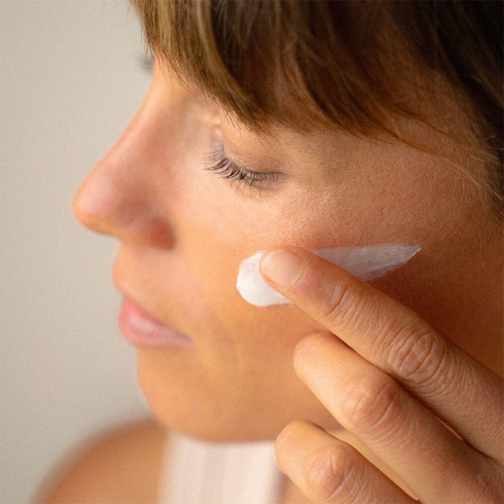 Frau trägt Creme auf die Wange auf. Weiße Creme auf der Haut. Nahaufnahme.