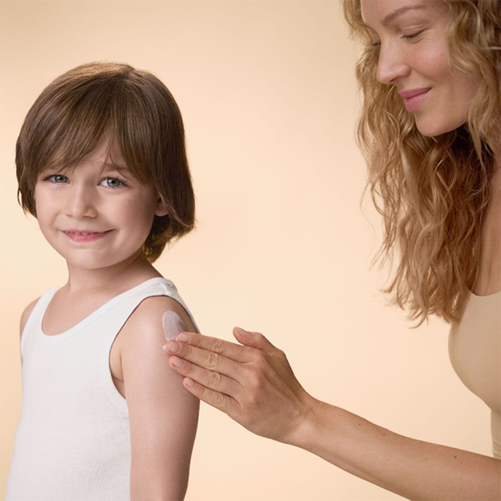 Femme appliquant de la crème sur le bras d'un enfant. Enfant portant un débardeur blanc.